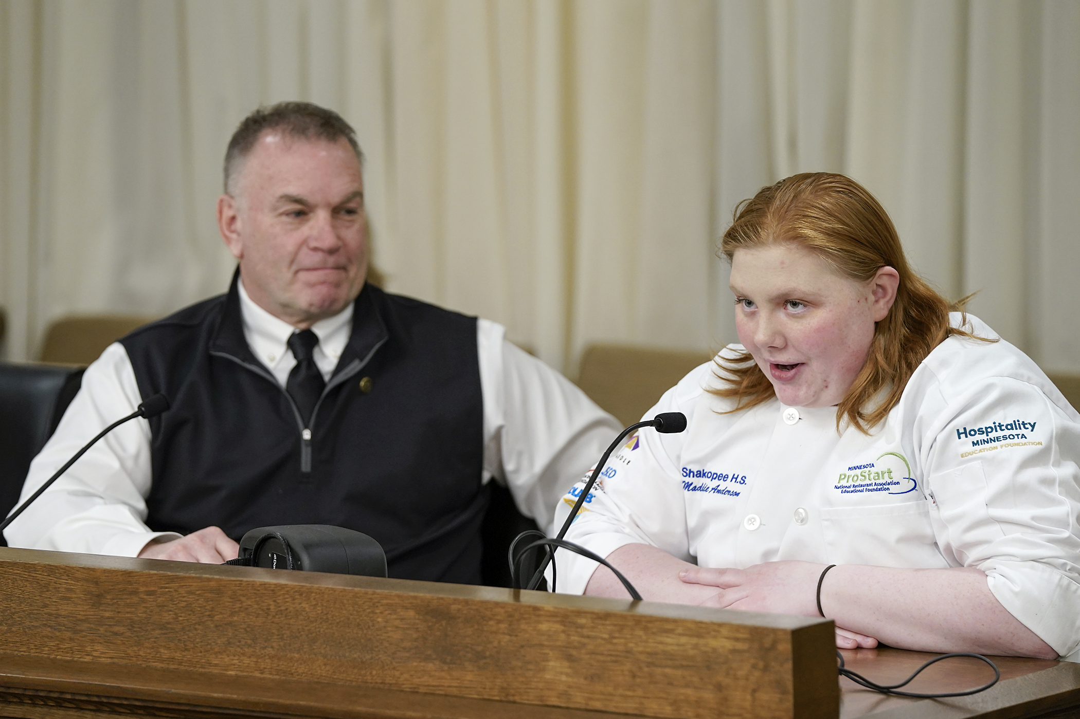 Madolyn Anderson, a former Shakopee ProStart student, tells the House workforce committee about her experience in the culinary arts and restaurant management program for high school students. Rep. Dave Baker, left, sponsors HF 961 that would fund a grant program for hospitality education. (Photo by Michele Jokinen)